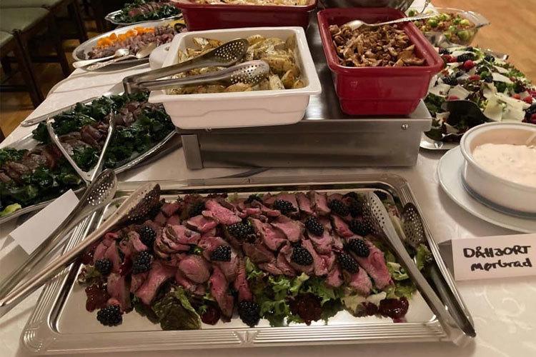 Et festbord med ulike retter, inkludert roastbiff med bær, salater og pasta i serveringsfat.