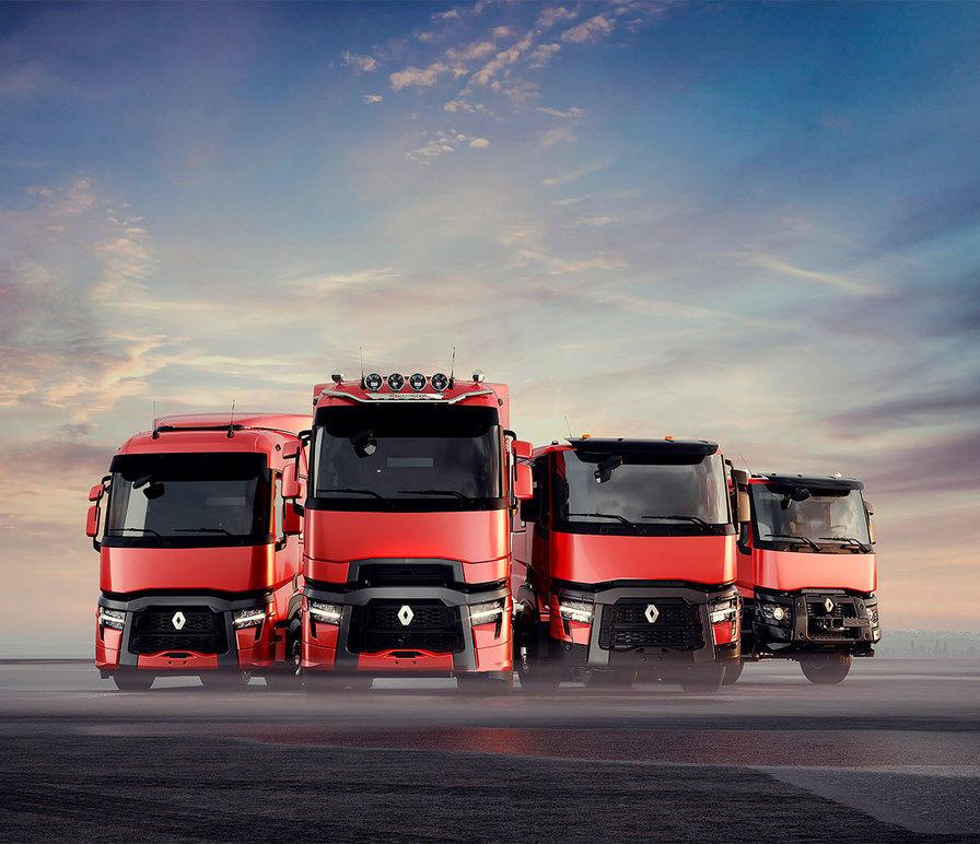 Fire røde Renault lastebiler står på en vei under en blå himmel med skyer.