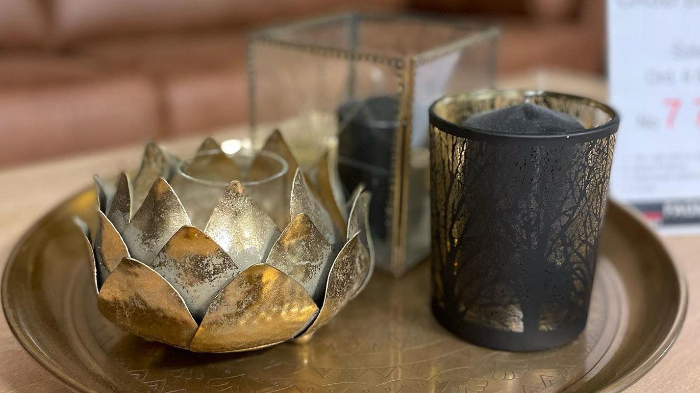 En dekorativ lysestake i gullformet lotus, en svart lysestake og en glassbeholder på et sølvfat.