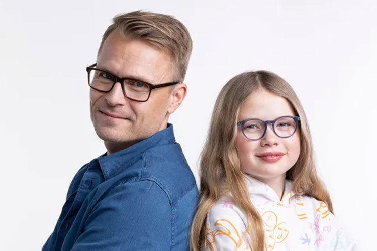 En voksen mann og en jente står rygg mot rygg, begge med briller og smilende ansikter.