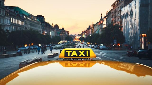 Utsikt fra en taxi med taklys, som viser en gate i byen ved solnedgang.