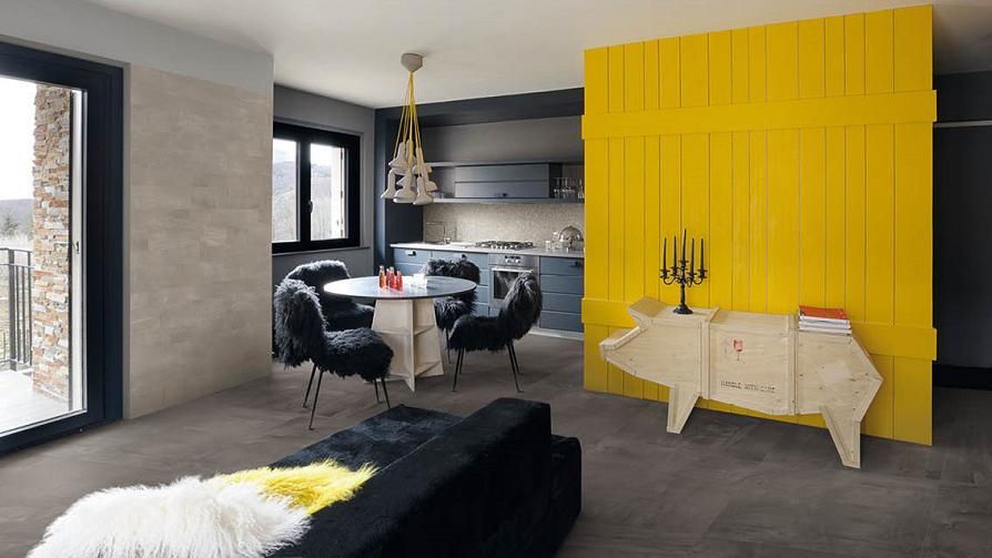 Moderne stue med gule vegger, svart sofa, spisebord med stoler og et stilrent skap.