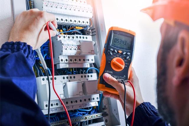 En elektriker bruker et multimeter for å teste elektriske forbindelser i et sikringsskap.