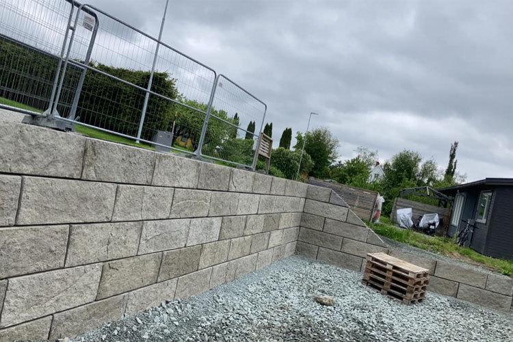 En mur av betongblokker med et gjerde i bakgrunnen, omgitt av grus og paller på byggeplassen.