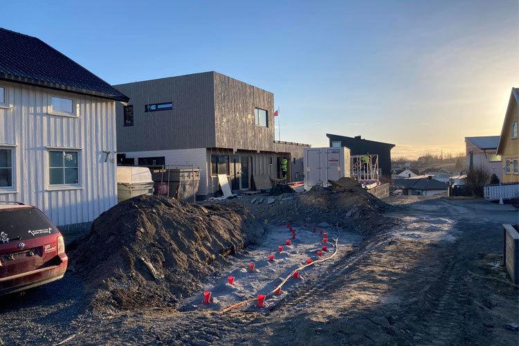 Byggeplass med flere hus under oppføring, grusvei og jordhauger i sollys.