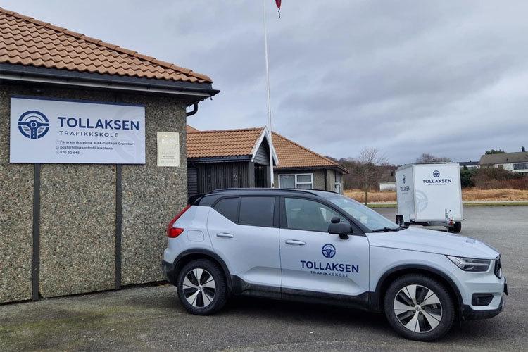 En grå Volvo XC40 parkert foran Tollaksen bygning med skilt og flagg.