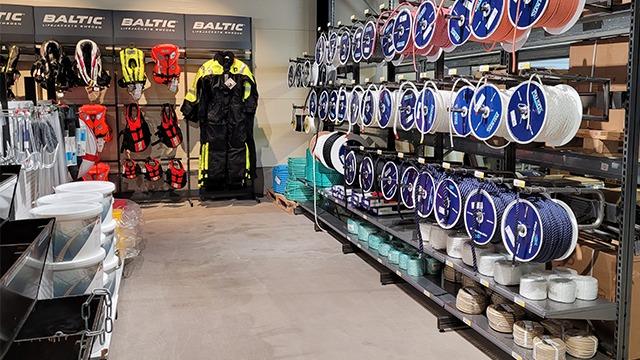 Butikkinnredning med BALTIC-seilutstyr, sikkerhetsvester og diverse tauverk på hyller.