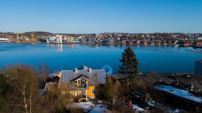 Utsikt over en by med en gul bygning i forgrunnen og en rolig innsjø i bakgrunnen.