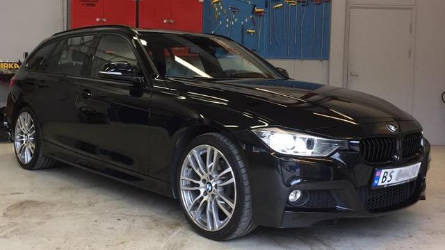 En svart BMW stasjonsvogn med aluminiumsfelger, parkert i en garasje med verktøy i bakgrunnen.