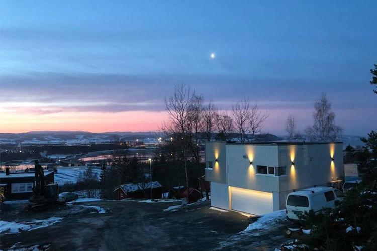 Moderne hus med lys i skumringen, omringet av snø og en vakker solnedgang i bakgrunnen.