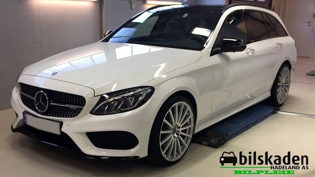 En hvit Mercedes-Benz stasjonsvogn med sportlige detaljer står på en løfteplattform i et verksted.