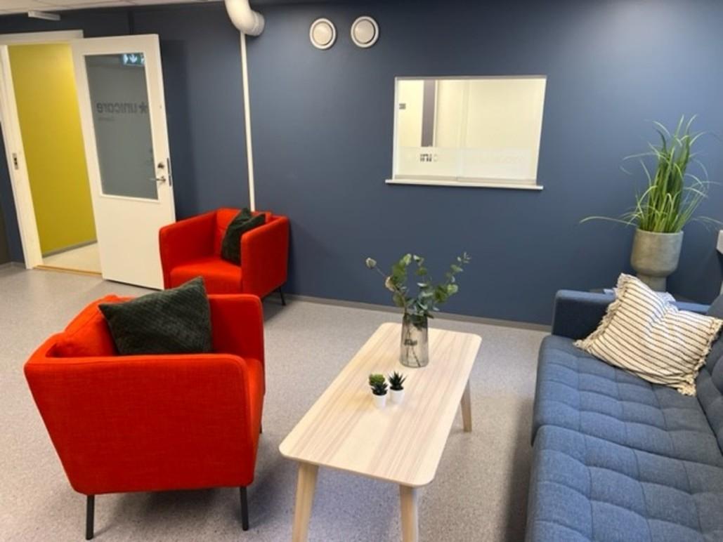 Moderne stue med røde og blå stoler, et lyst bord og en plante på veggen. Veggene er blå med speil og dør.