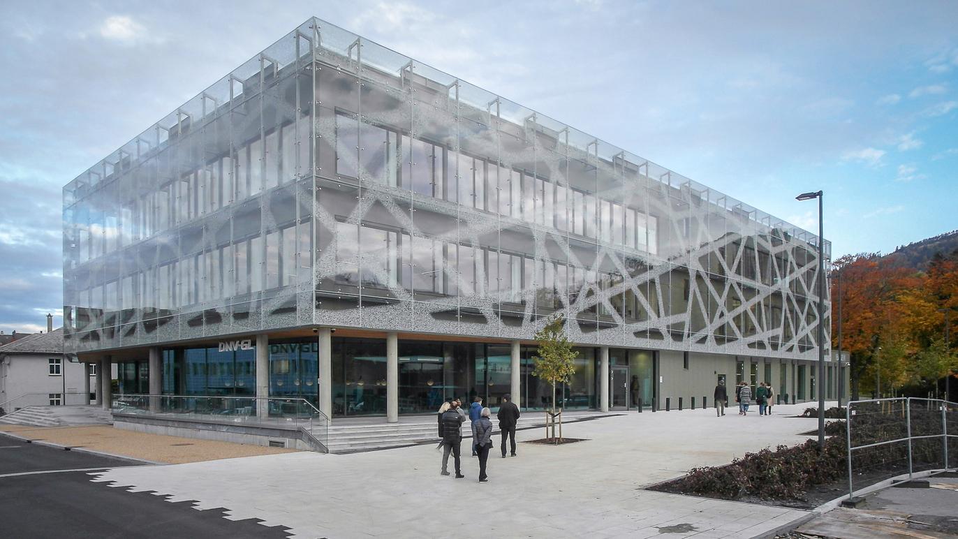 Moderne kontorbygg med glassfasade og geometrisk design, omgitt av trær og gangveier.