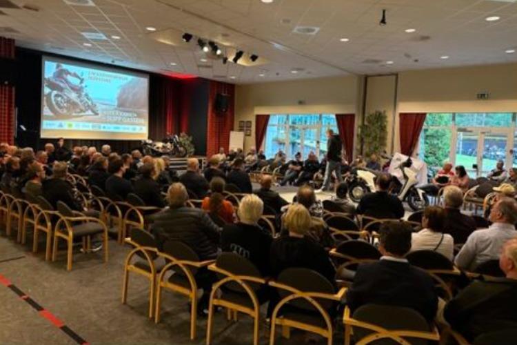 En stor forsamling av mennesker sitter i et rom med en presentasjon på skjermen.