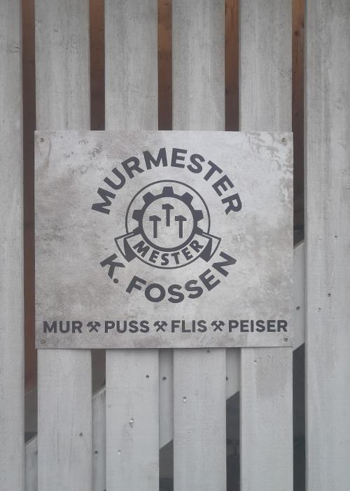 Skilt med teksten "Murmester K. Fossen" og symboler for mur, puss, flis og peiser på en trevegg.
