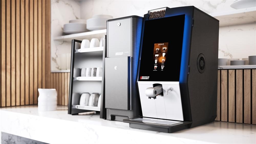 Kaffemaskin med moderne design og skjerm, plassert på en marmorbenk med kopper i bakgrunnen.
