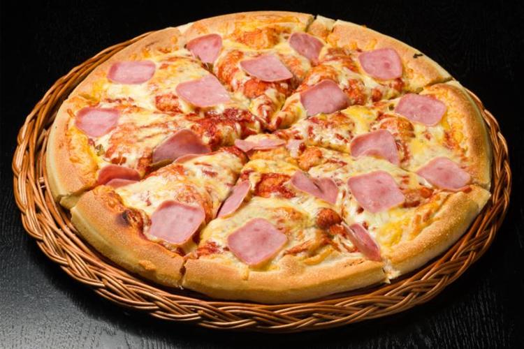En stor pizza med skinke og ost, servert på en flettet kurv.