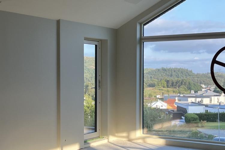 Lys og moderne stue med store vinduer som gir utsikt over landskapet og bygningene utenfor.