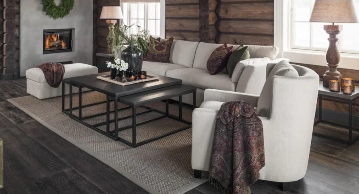 Moderne stue med en lys sofa, bord, lamper og peis i en hytte med trevegger.