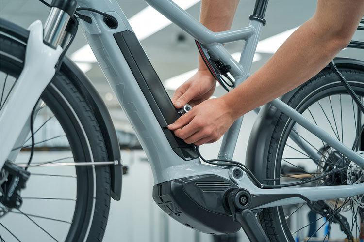 En person installerer et batteri på en elektrisk sykkel i et verksted.