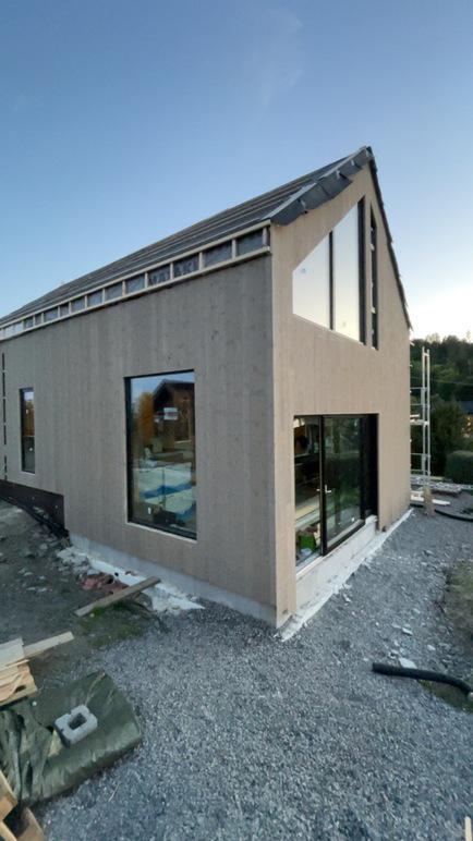 Moderne hus med store vinduer og solcellepaneler, plassert på en gruslagt tomt.