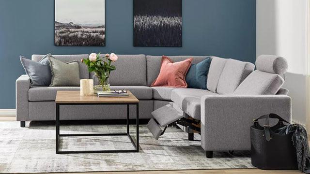 Moderne stue med grå sofa, bord i tre, puter i forskjellige farger og blomster i vase på bordet.