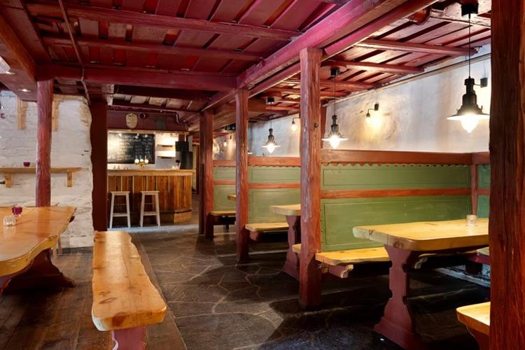 Koselig restaurantinteriør med trebenker, bord og belysning i en historisk atmosfære.
