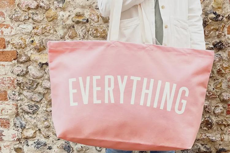 En person holder en stor rosa veske med teksten "EVERYTHING" på en steinvegg.