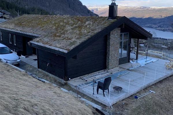 Hus med torvtak og steinvegg, beliggende i fjellandskap med utsikt over innsjø.