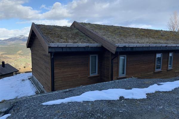 Hus med torvtak og trepanel, beliggende i fjellandskap med snø og fjell i bakgrunnen.