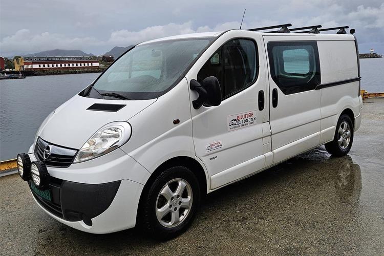 Hvit varebil parkert ved vannkanten med takstativ og logo på siden.
