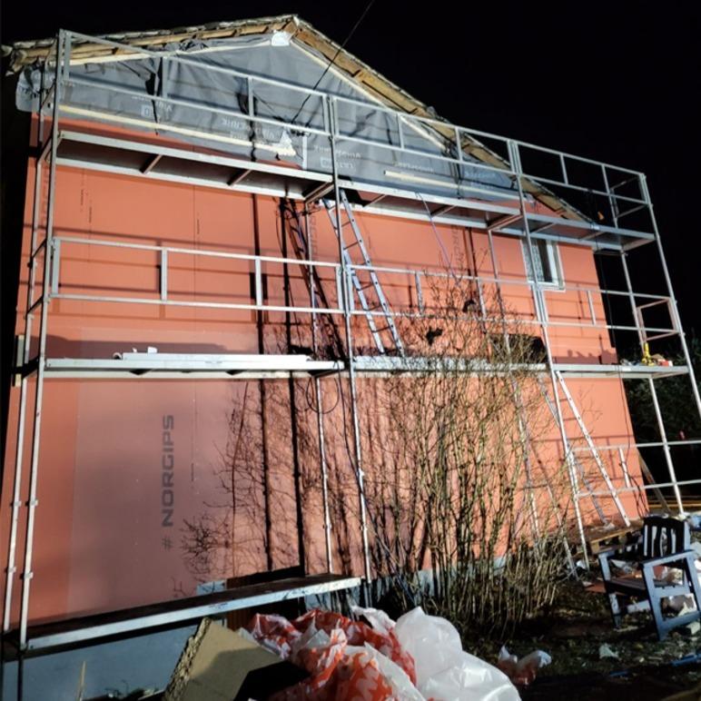 Hus med rosa vegger og stillas rundt, klart for oppussing, med verktøy og materialer i nærheten.