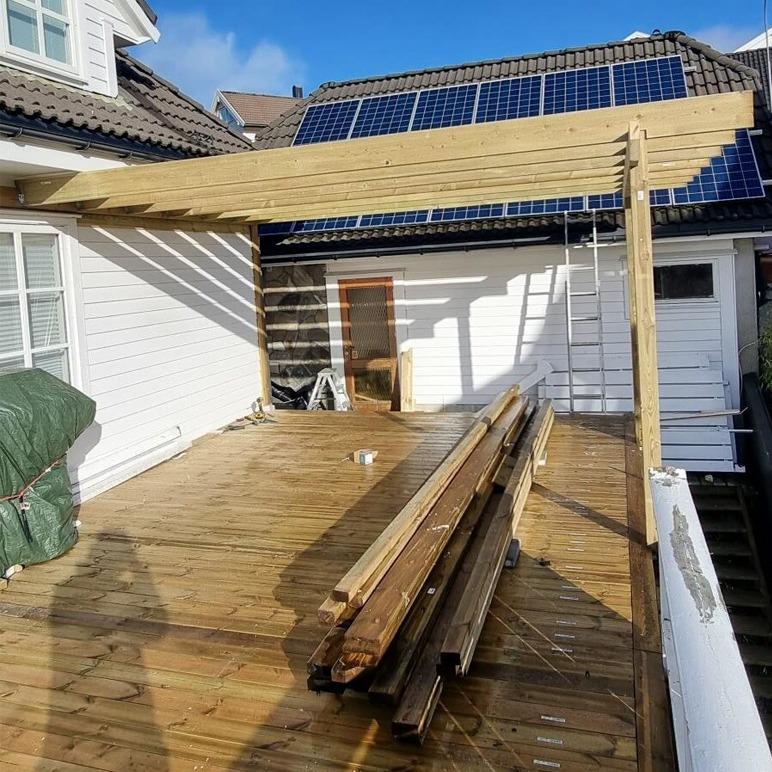 Terrasse med solcellepaneler, treverk og byggeutstyr under konstruksjon.