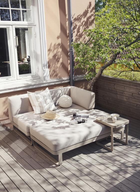 En koselig uteplass med en moderne sofa, et lite bord og skygger fra trærne.