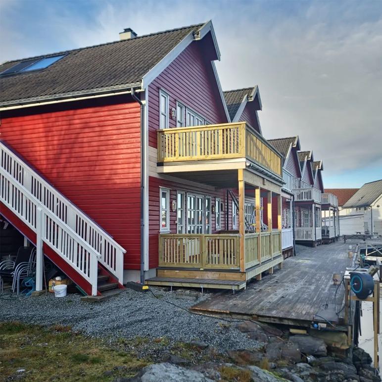 Røde hus med balkonger ved vannkanten, omgitt av grus og treplanker.