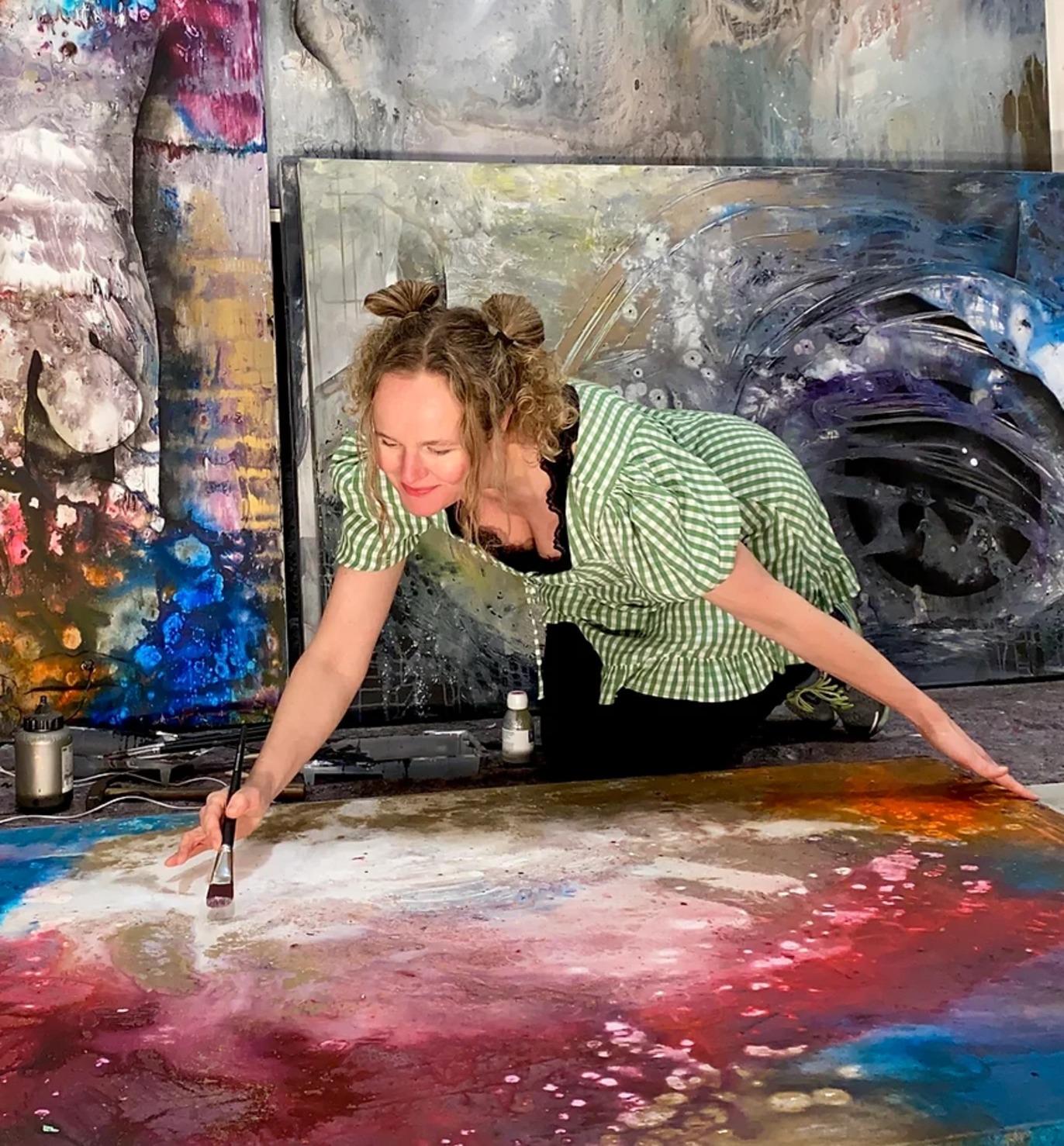 Kvinne i grønn rutete skjorte maler på et stort lerret med fargerike penselstrøk i et kunstnerisk studio.