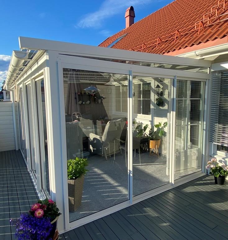 Lys og moderne vinterhage med glassvegger, møbler og planter på en terrasse med tredekk.