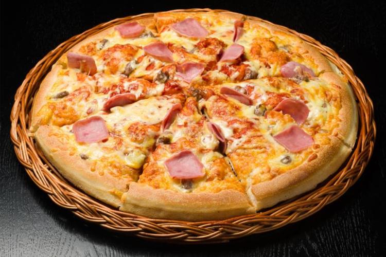En stor pizza med skinke, ost, sopp og tomatsaus, servert på en flettet kurv.