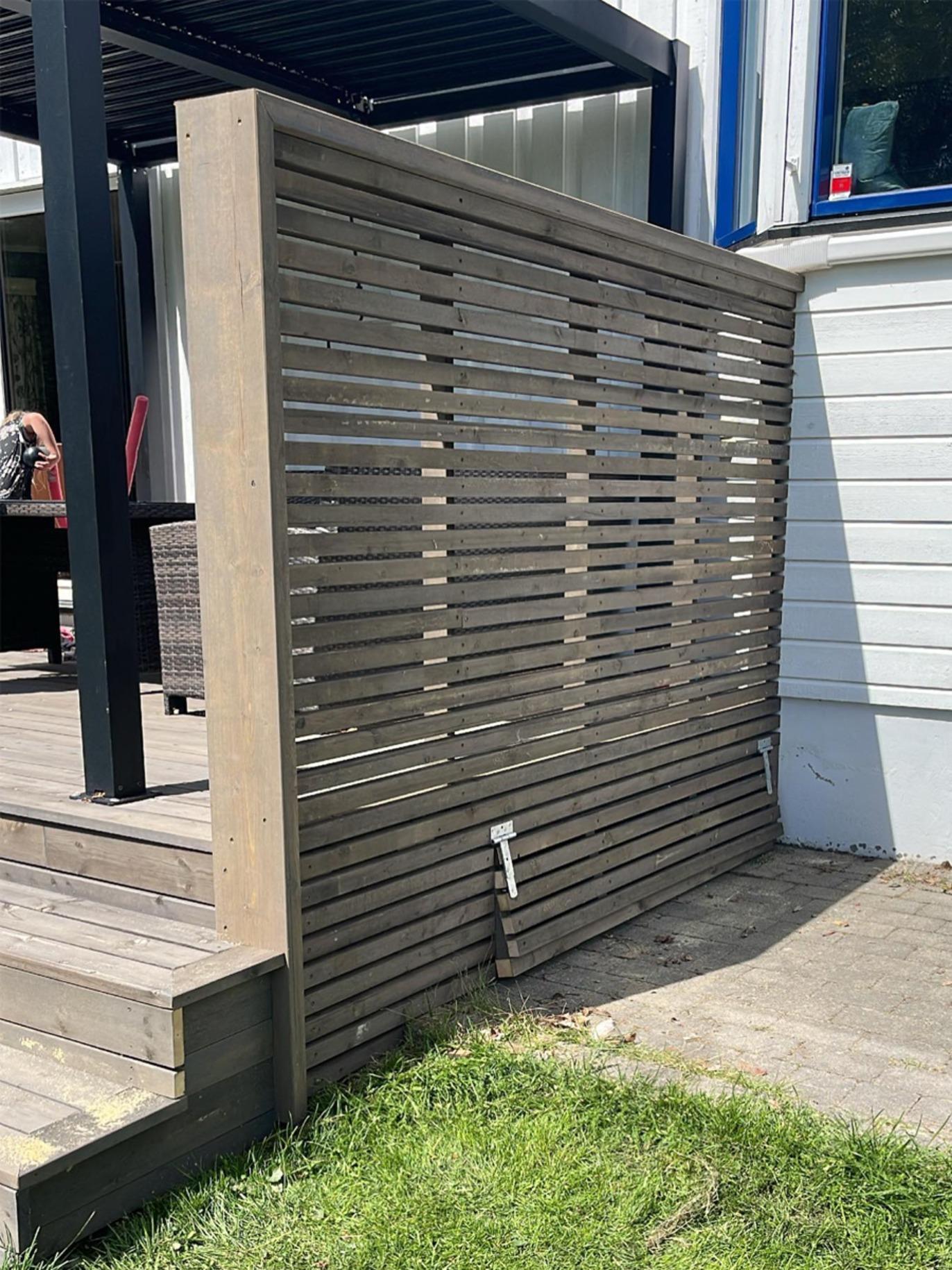 En moderne trevegg med horisontale spiler, plassert ved en terrasse med grønt gress.