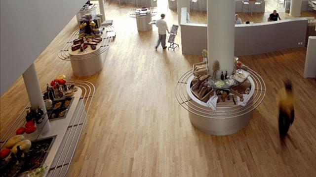 Moderne restaurantinnredning med treverk, bufféområde og ansatte som serverer mat.