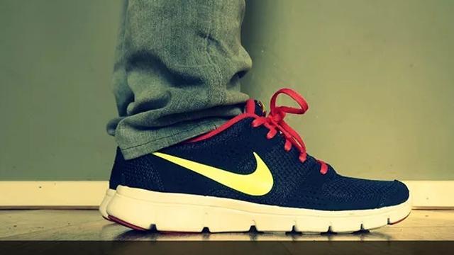 En person står med en fot i en svart Nike-sko med gule detaljer og røde snørebånd.