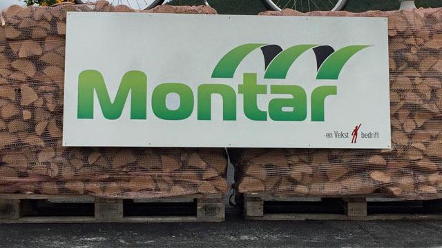 Montar-skjold med grønn og hvit tekst på en stor plakat, plassert foran stablet med steinblokker.