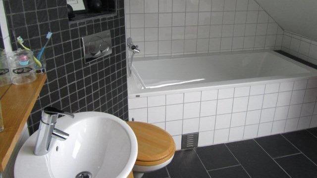 Moderne bad med badekar, servant og toalett, fliser i svart og hvitt, og tre detaljer.