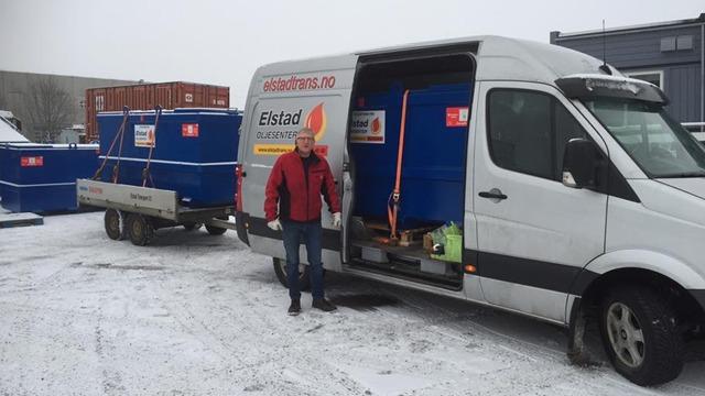 En mann står ved siden av en hvit varebil med blå containere på tilhenger, omringet av snø.