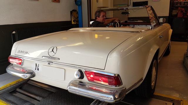 En hvit Mercedes cabriolet med en mann som sitter i førersetet, parkert i en garasje.