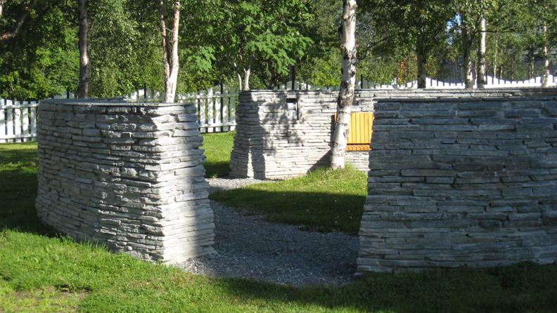 Stenmur med gangsti i en grønn park, omkranset av bjørketrær og benk til å sitte på.