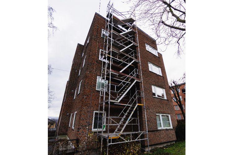En murbygning med stillas på siden, som viser pågående renovering av fasaden.