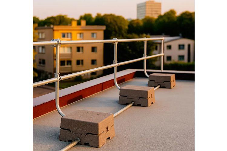 Railing med betongblokker på taket av en bygning, med leiligheter i bakgrunnen i solnedgang.