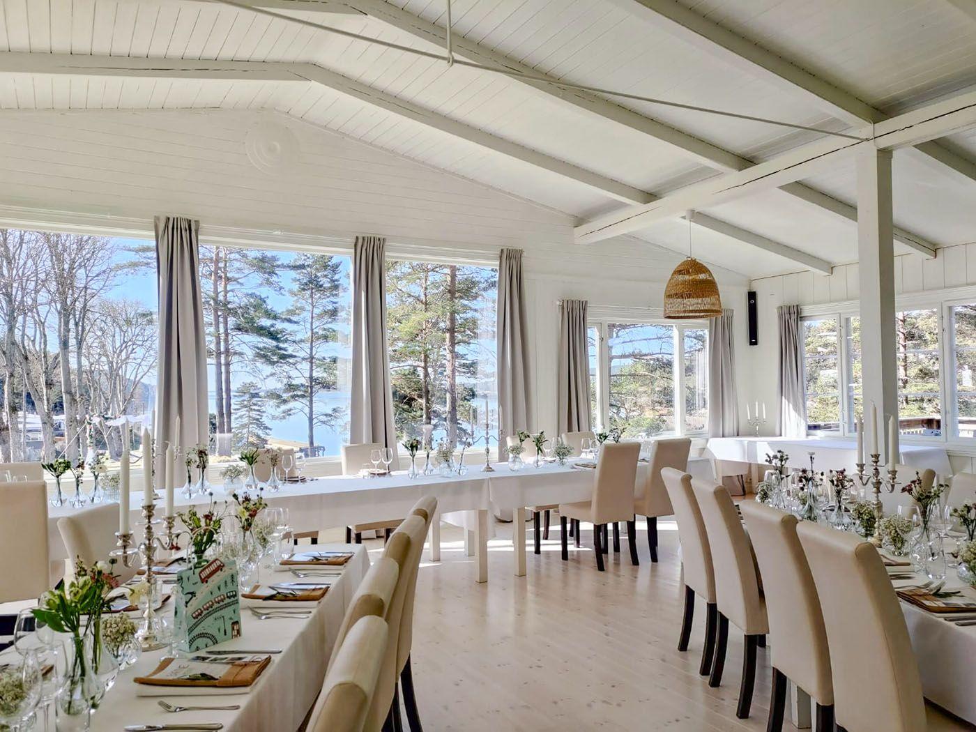 Lyst og moderne spiserom med langbord, stoler og vinduer som gir utsikt over naturen.