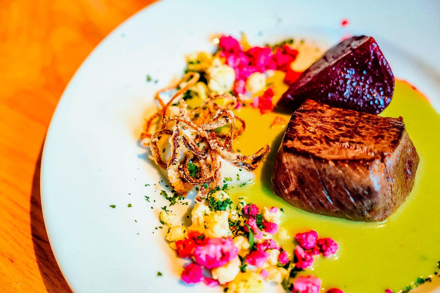 En tallerken med saftig biff, rødbeter, sprø løk og fargerike blomster, servert med en grønn saus.